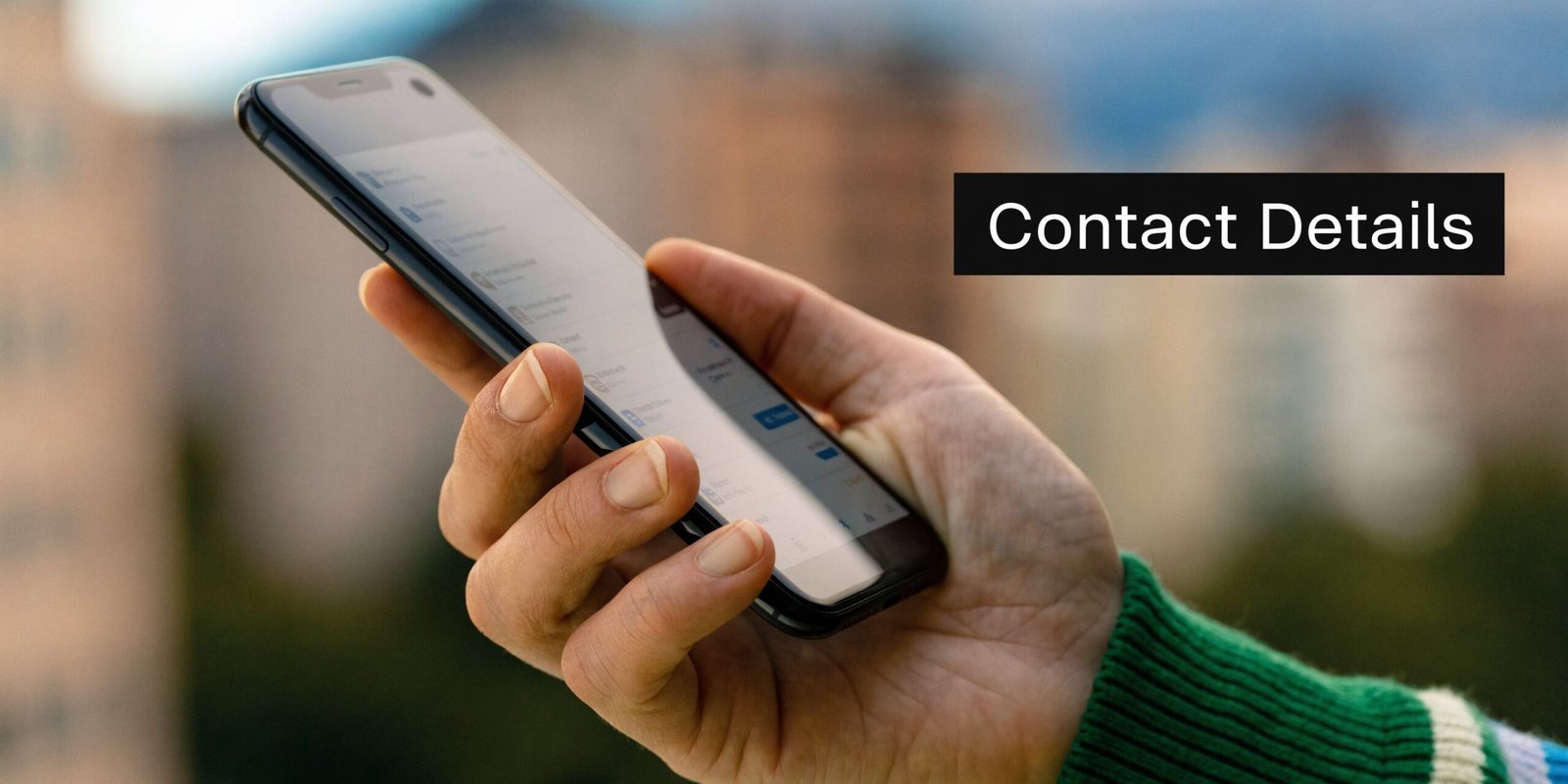 A close-up view of a person holding a smartphone showing contact list details outdoors in sunlight.