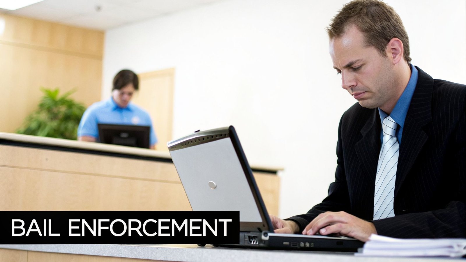 A man in a pinstripe suit and tie is intently working on a laptop, with "BAIL ENFORCEMENT" text.