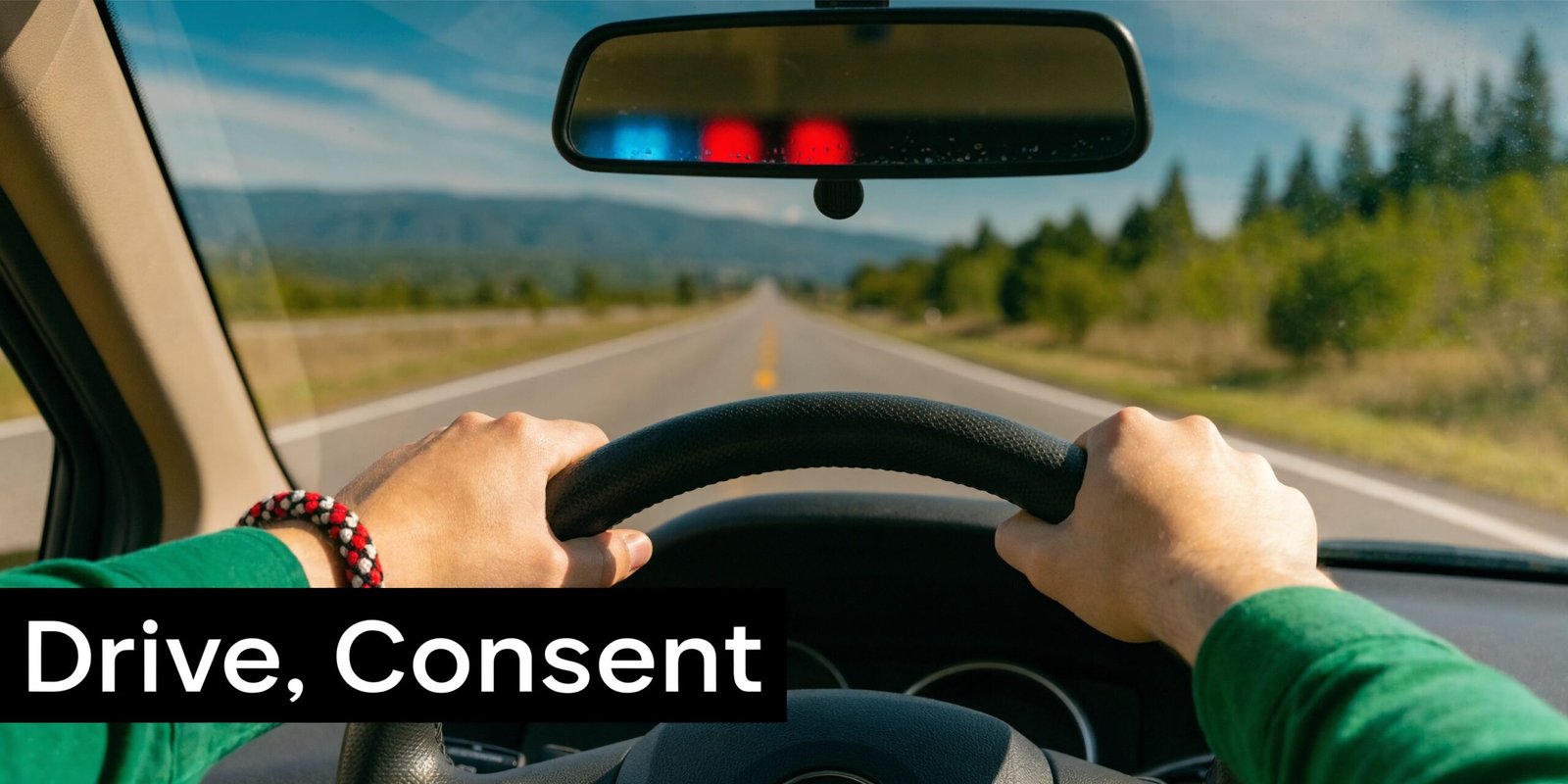A first-person view from inside a car with police lights visible in the rearview mirror on a road.
