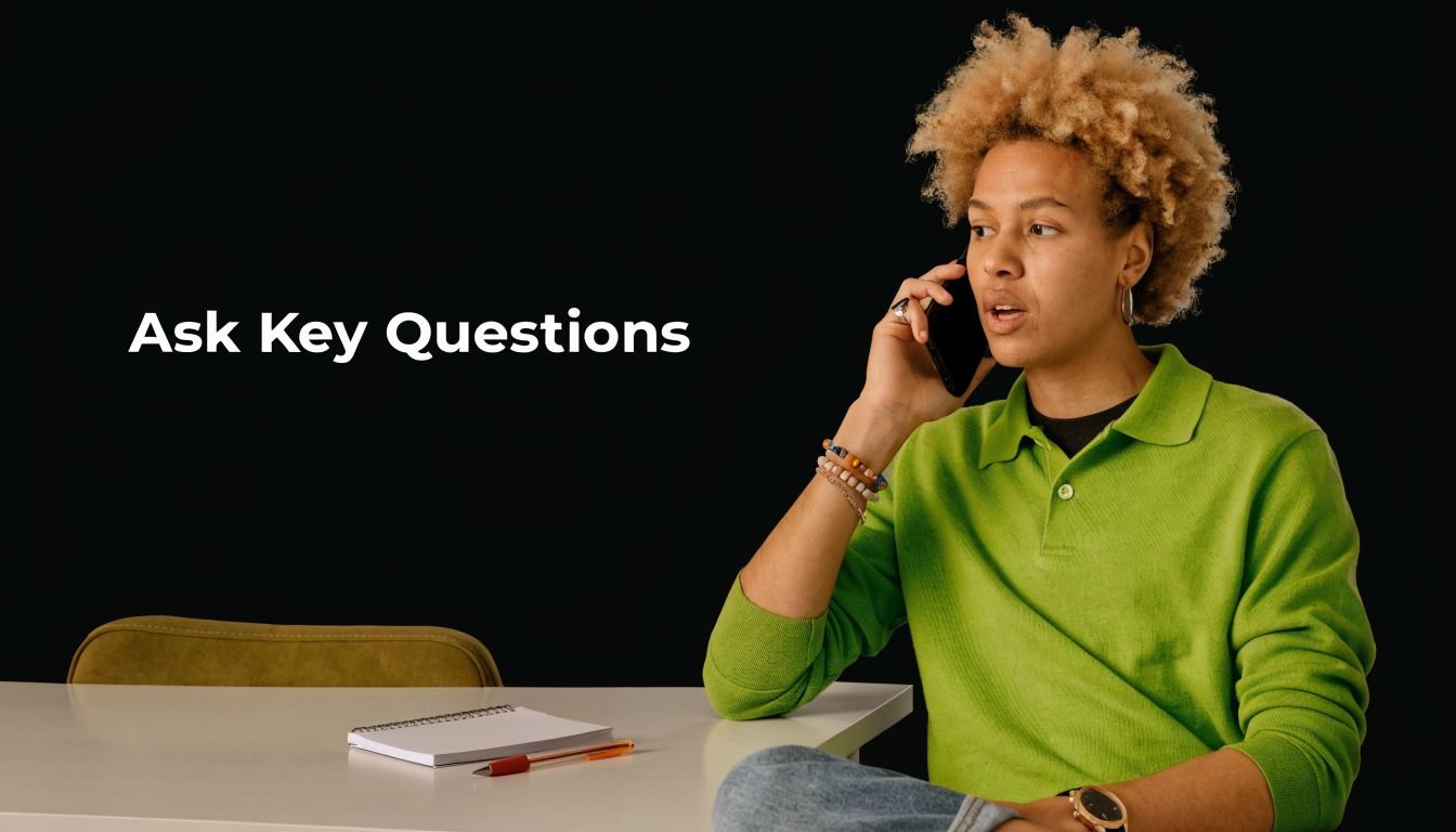A person with curly blonde hair wearing a bright green shirt talking on the phone at a desk.