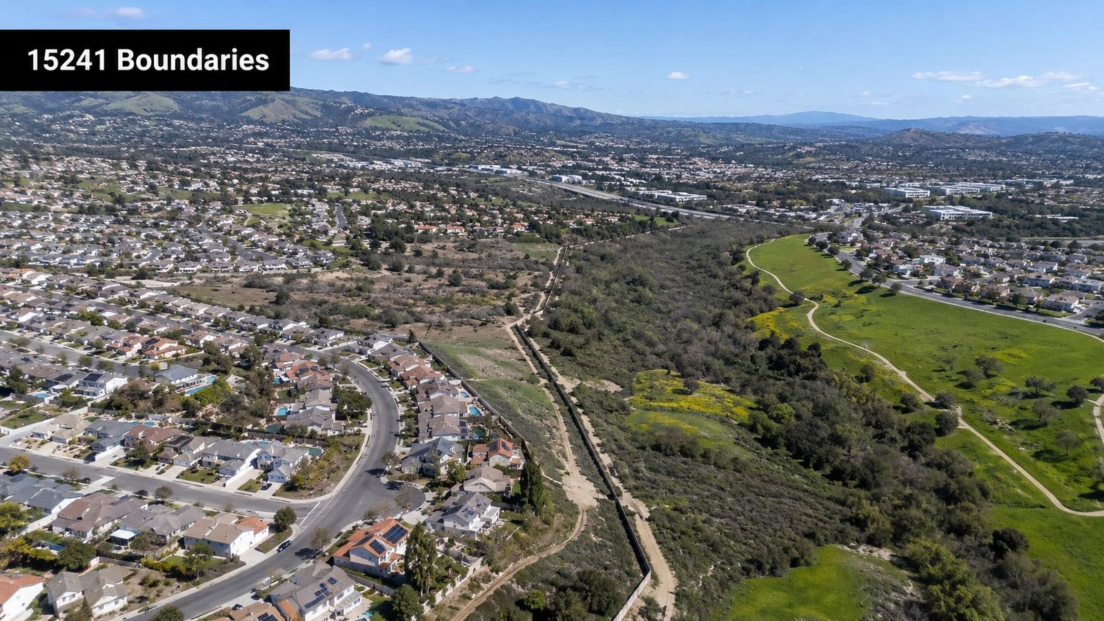 An aerial view of residential homes bordering a large, open green space and natural landscape.