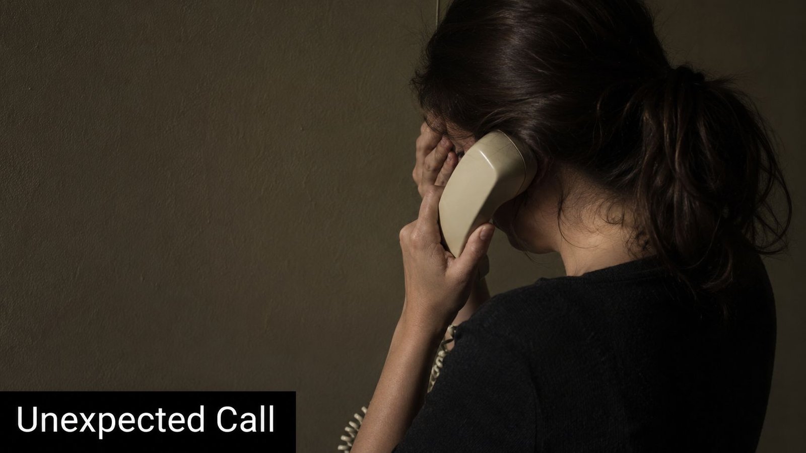 A distressed woman holding a landline phone to her ear while covering her face with her hand.